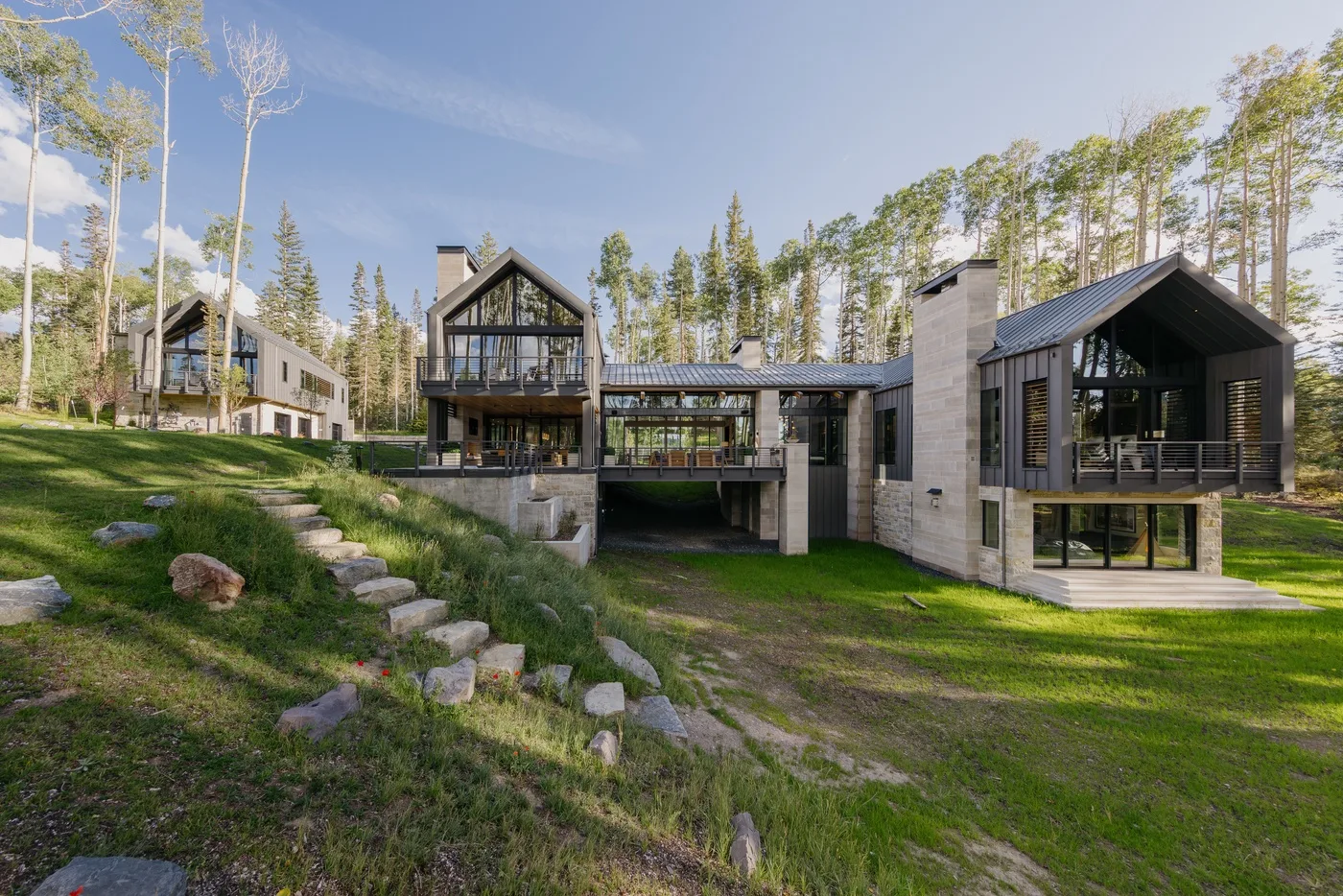 A modern house with large windows sits among trees on a grassy slope.