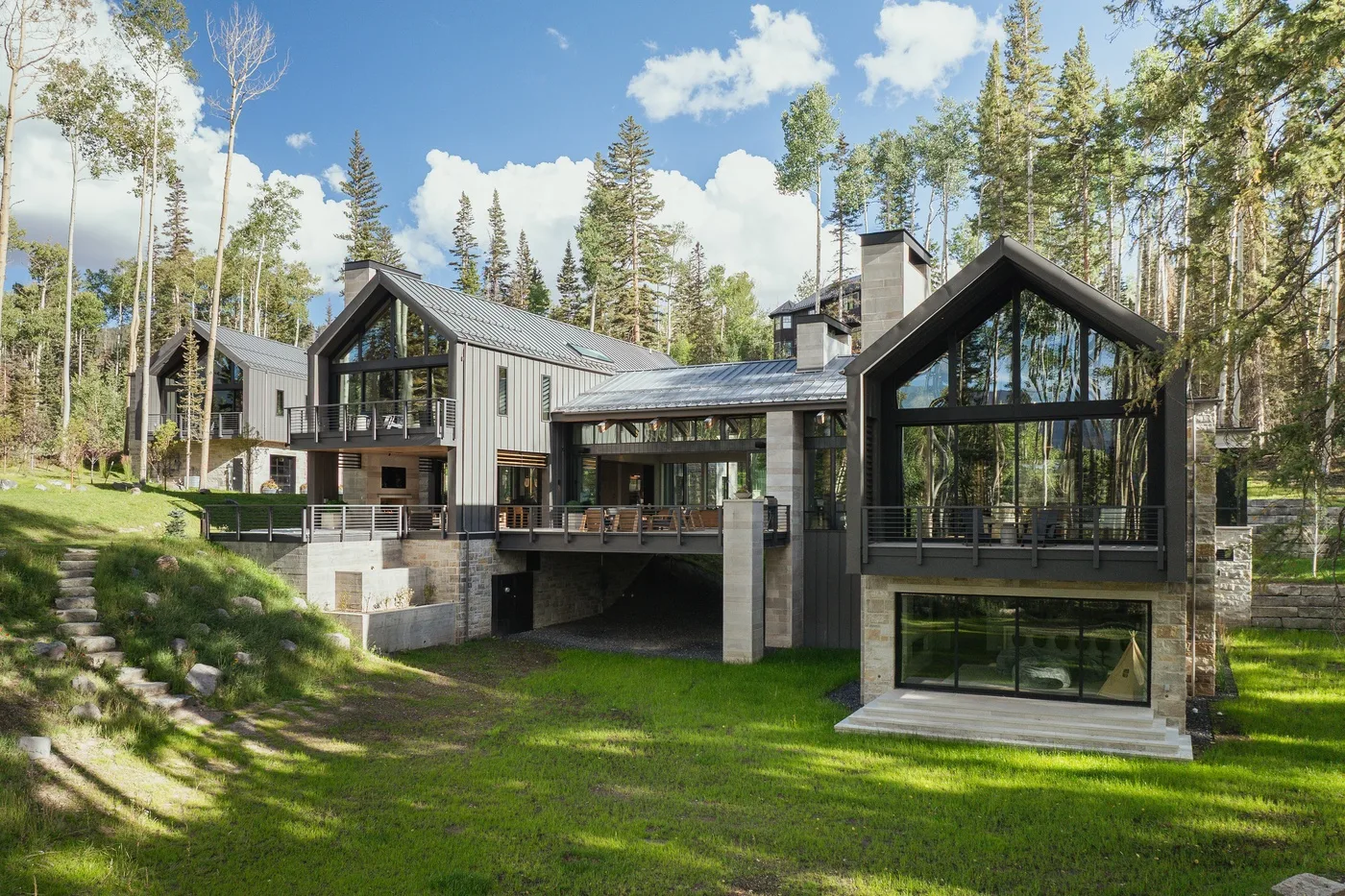 A modern house sits among tall trees, with expansive glass windows and a sloped roof.