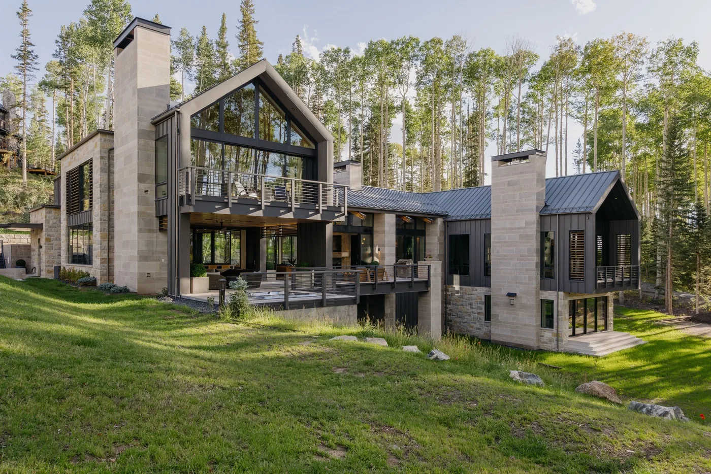 A modern house with large windows sits among trees on a grassy slope.