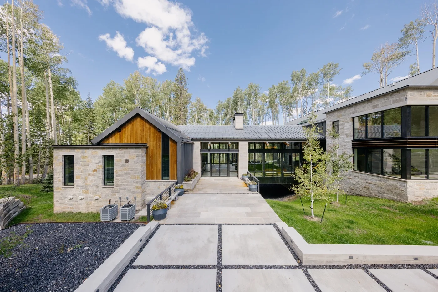A modern home with stone walls and large windows sits beside a landscaped yard.