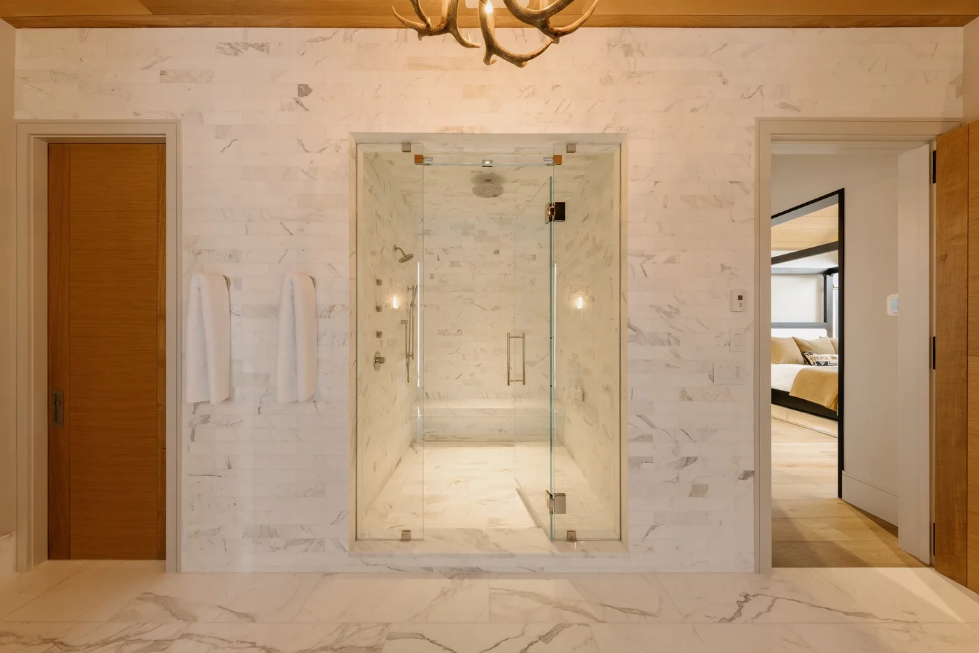 A bright bathroom features a glass shower and pale stone surfaces.