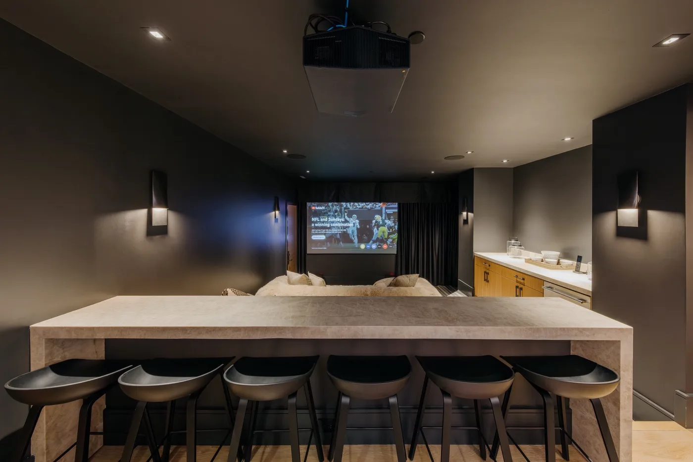 A home theater with a large screen, seating, and a counter with stools.