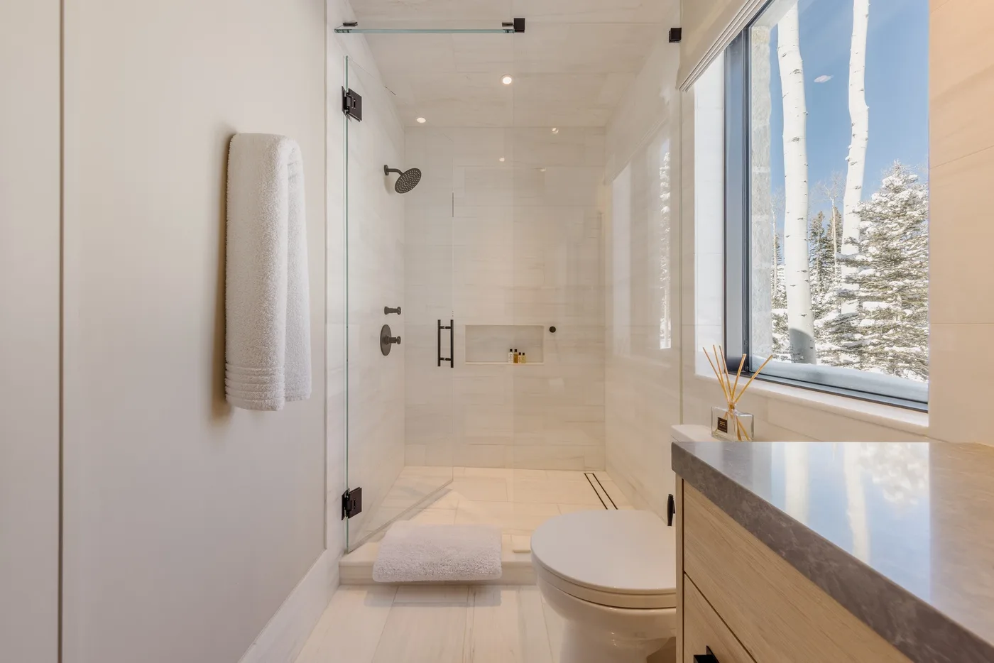 A bright bathroom with a glass shower, toilet, and large window.