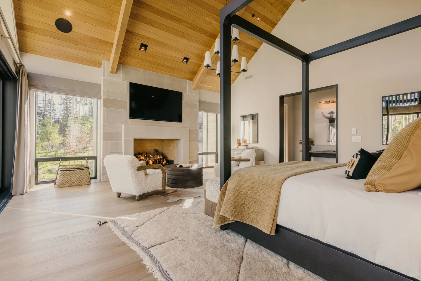 A bedroom with a large bed, fireplace, and television beneath a vaulted wood ceiling.