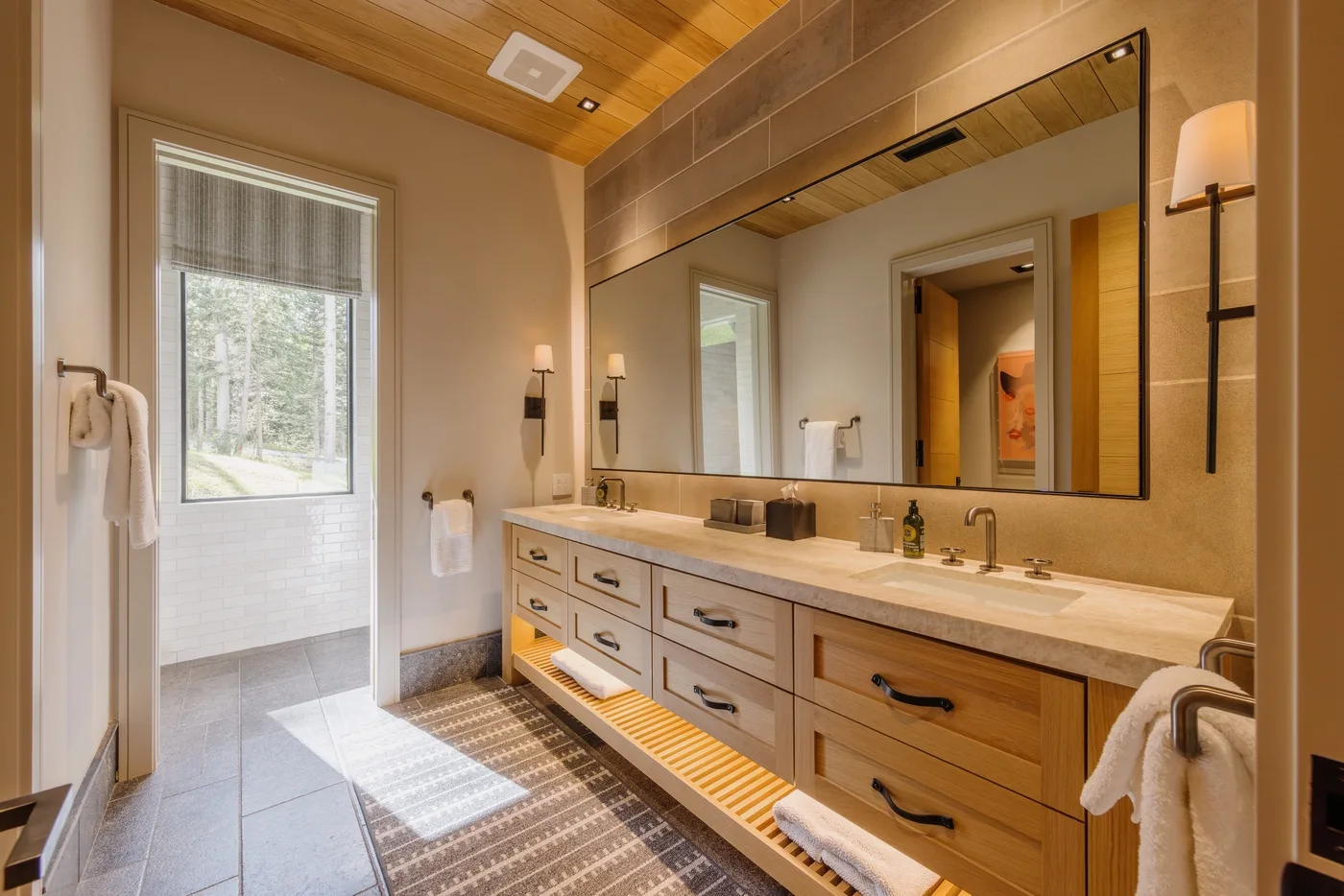 A spacious bathroom with a long vanity, broad mirror, and large window.