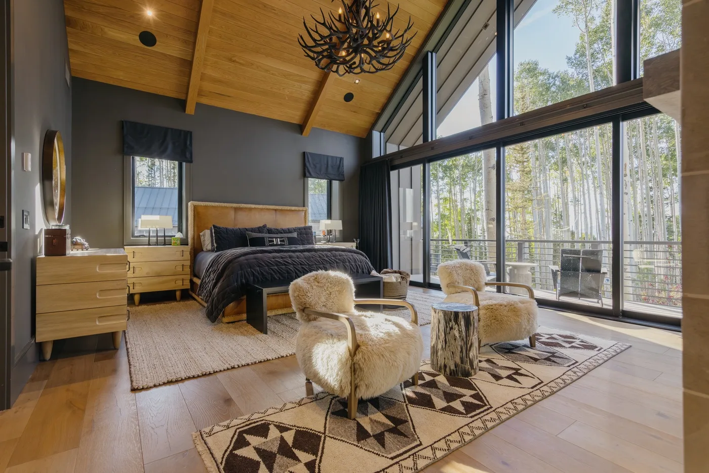 A spacious bedroom with a bed, lounge seating, and large windows overlooking trees.