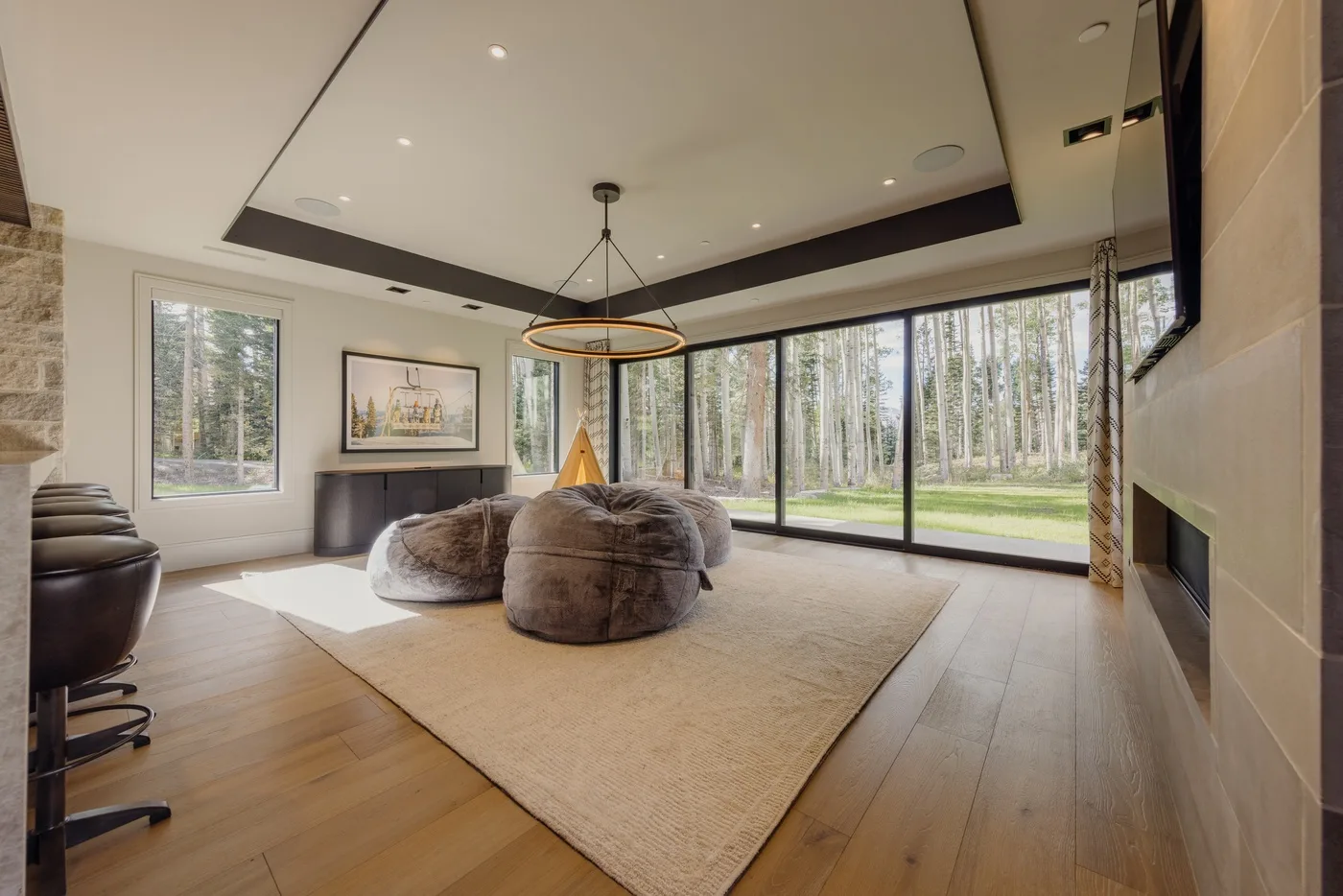 A spacious living room with low seating and floor-to-ceiling windows overlooking trees.