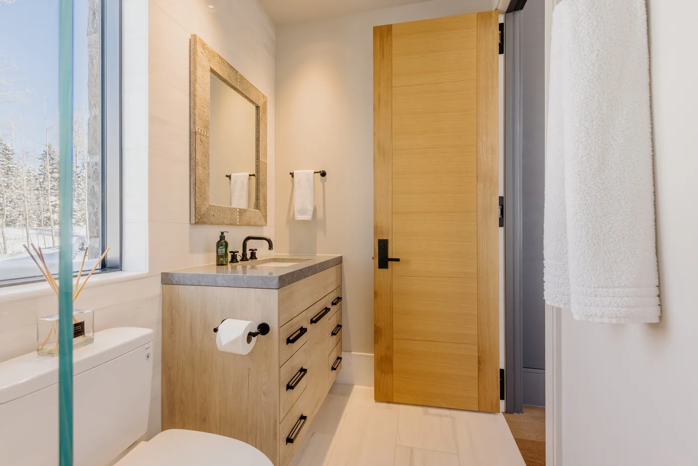 A bright bathroom with a wood vanity and a glass shower screen.