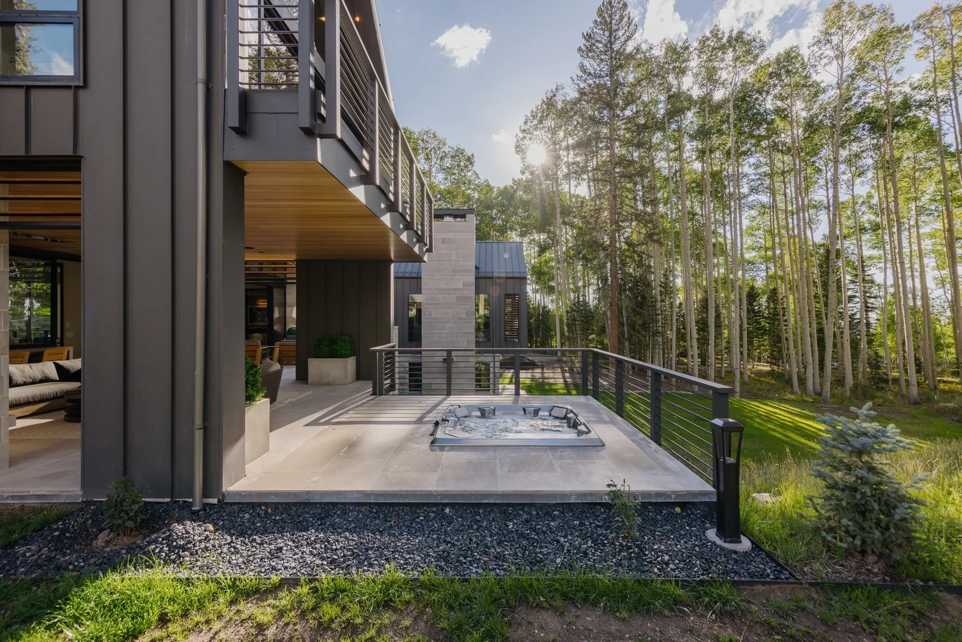 A modern house opens onto a patio with an outdoor hot tub and surrounding trees.
