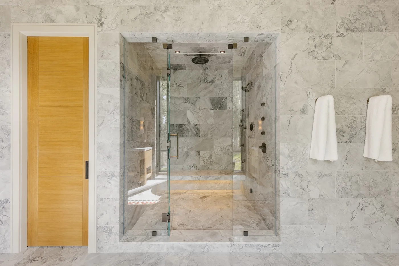 A marble bathroom with a glass shower and two white towels hanging on the wall.