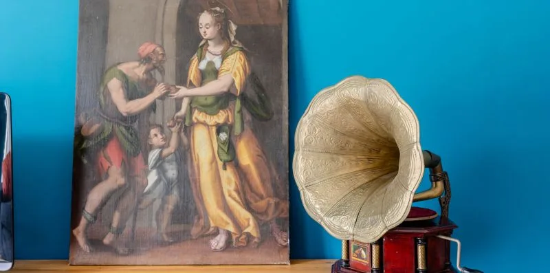 Una pintura se apoya en una pared azul brillante junto a un gramófono antiguo.