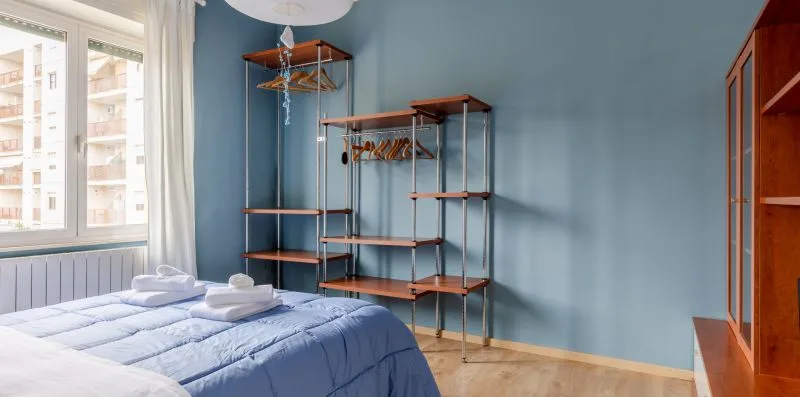 Un dormitorio con una cama azul y estantes abiertos junto a una pared azul.