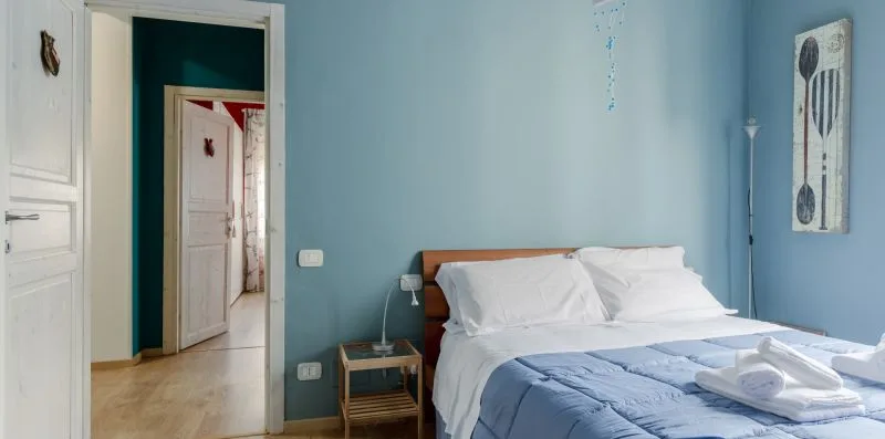 Un dormitorio con una cama, ropa de cama azul y paredes azul claro.