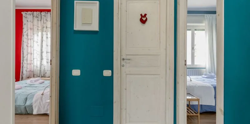 Un pasillo de color turquesa con una puerta blanca y dormitorios a ambos lados.
