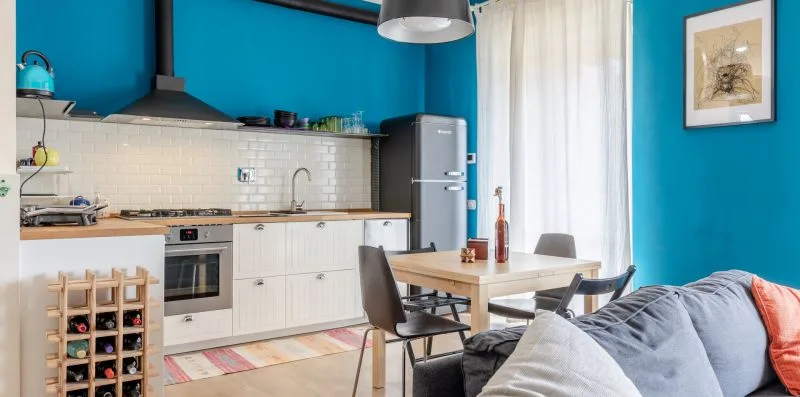 Una cocina y comedor con armarios blancos y una mesa junto a una pared azul.