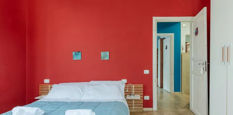 Un dormitorio con una cama junto a una pared roja y una puerta abierta.