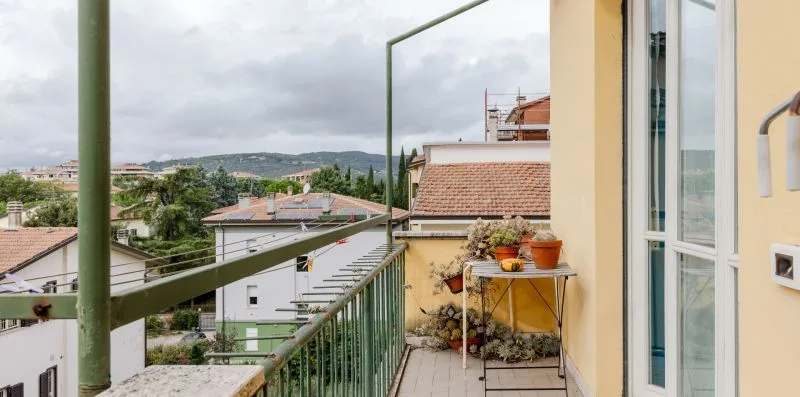 Un balcón estrecho con barandillas metálicas da a casas cercanas y zonas verdes.