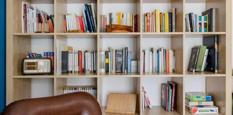 Una estantería llena de libros, con una radio y un asiento de cuero delante.