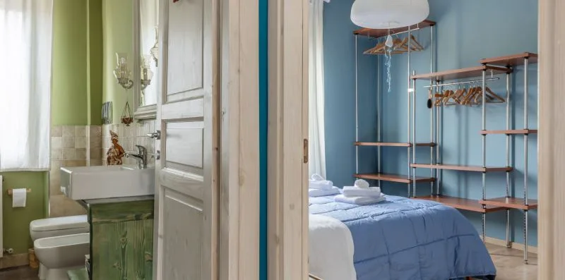 Un dormitorio con ropa de cama azul y percheros abiertos junto a un baño.