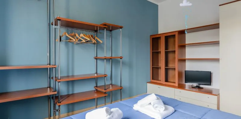 Un dormitorio con una cama azul y estanterías abiertas de madera junto a las paredes.