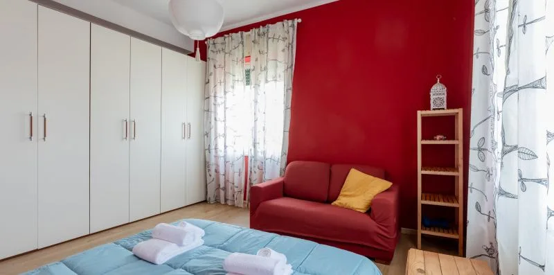 Un dormitorio con una cama, un sofá rojo y armarios blancos.
