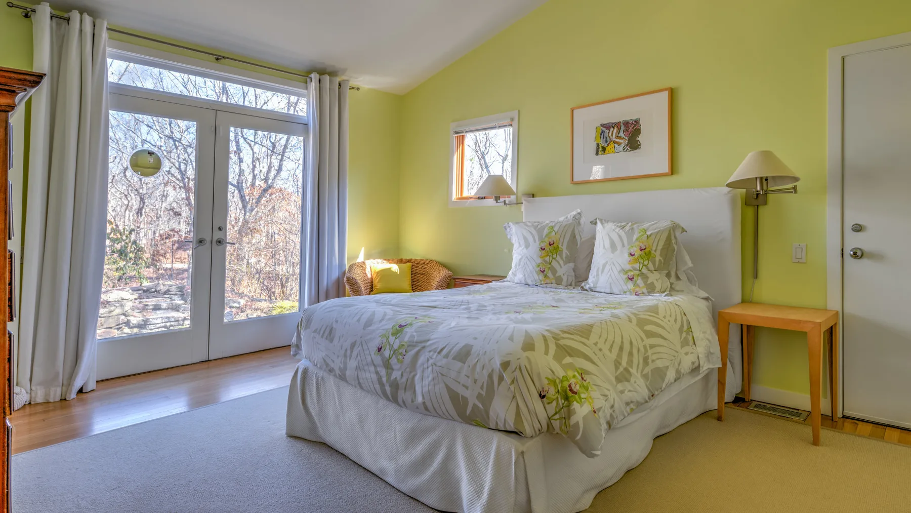 A bedroom with a neatly made bed beside tall glass doors.