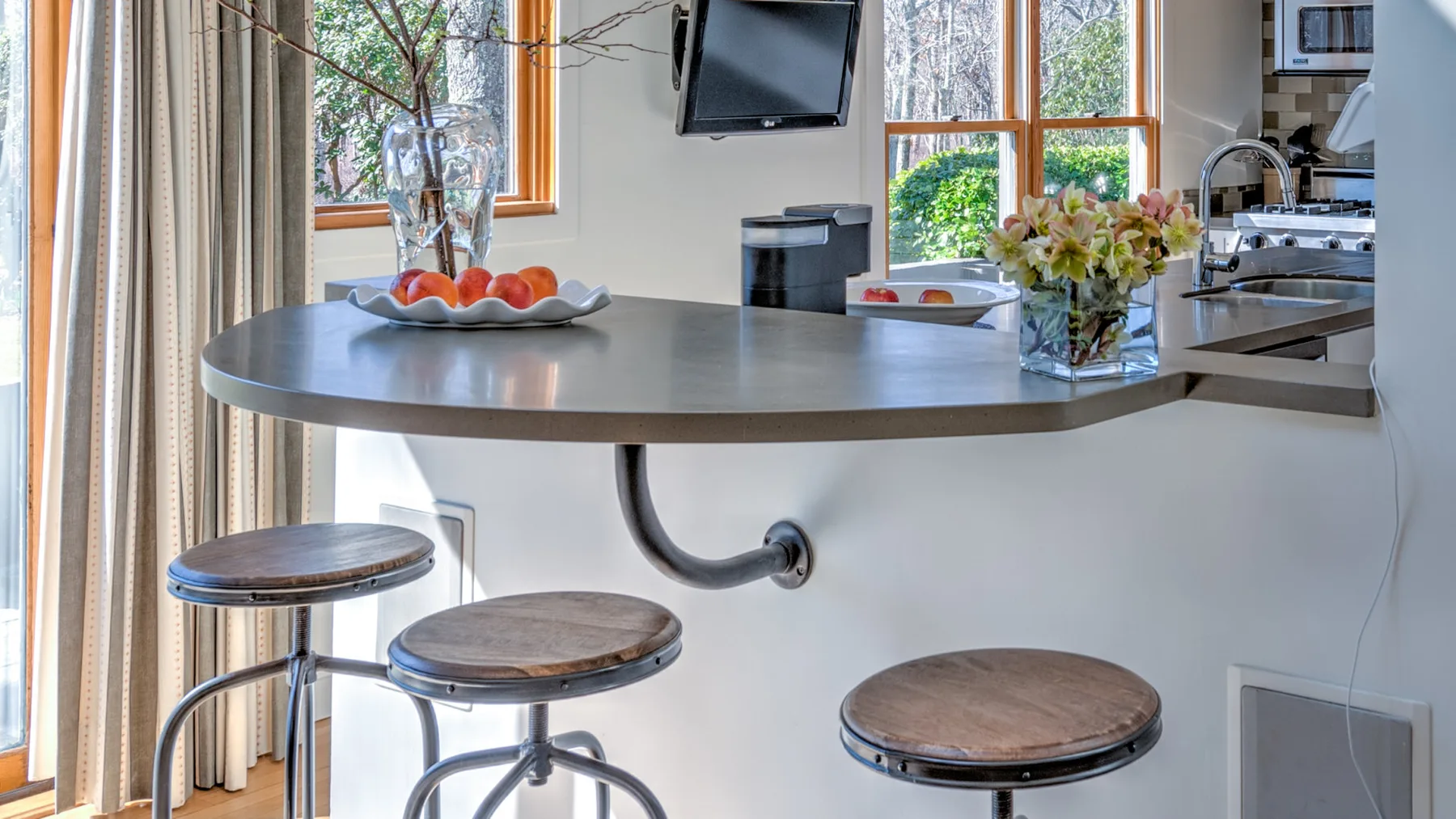 A bright kitchen with a curved counter, three stools, and large windows.