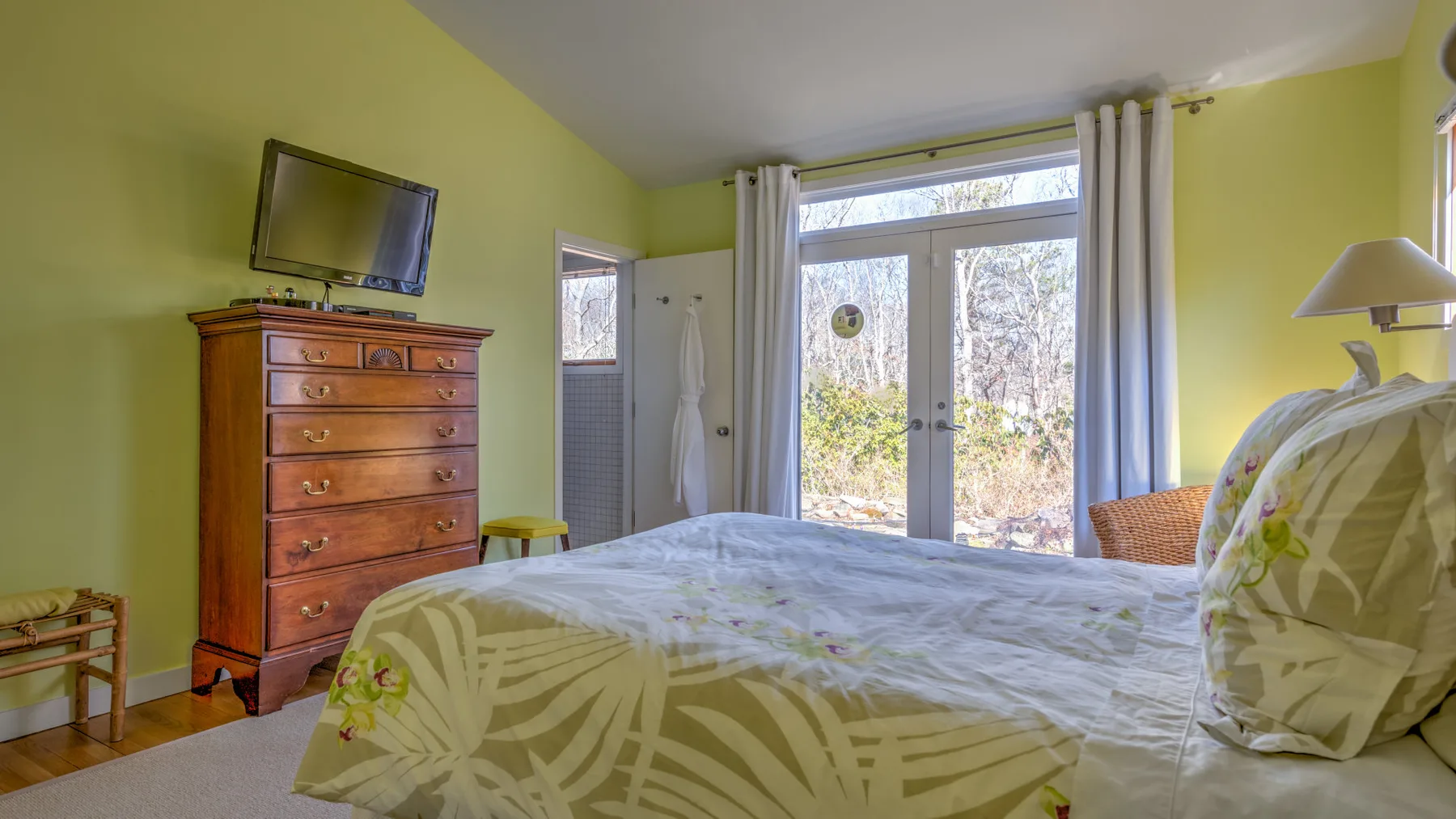 A bright bedroom with a bed and glass doors opening onto a garden.