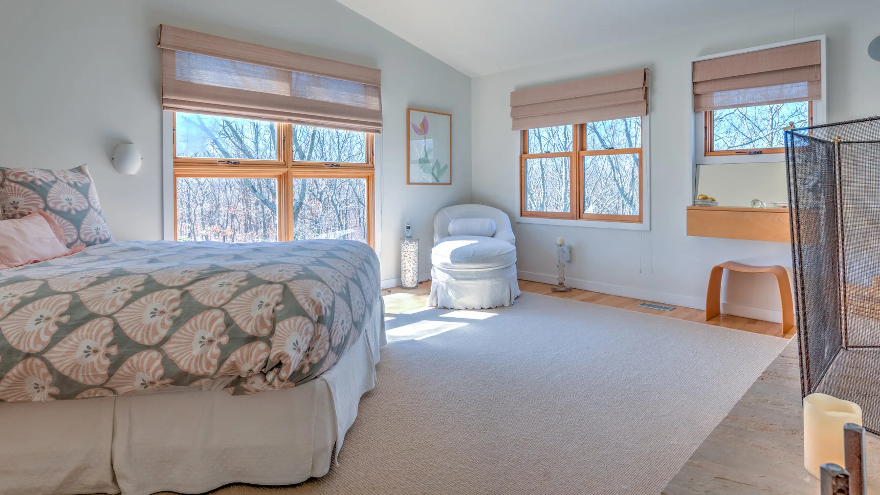 A bright bedroom with a bed, armchair, and windows overlooking trees.