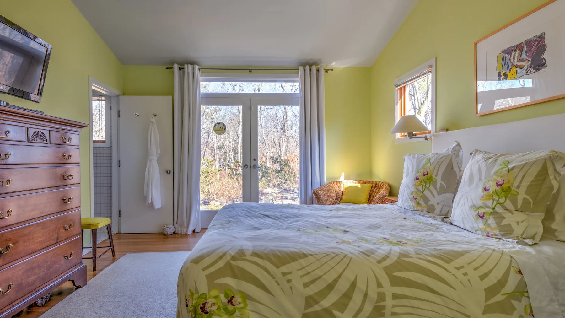 A bedroom with a large bed, patterned bedding, and glass doors opening to a view outside.