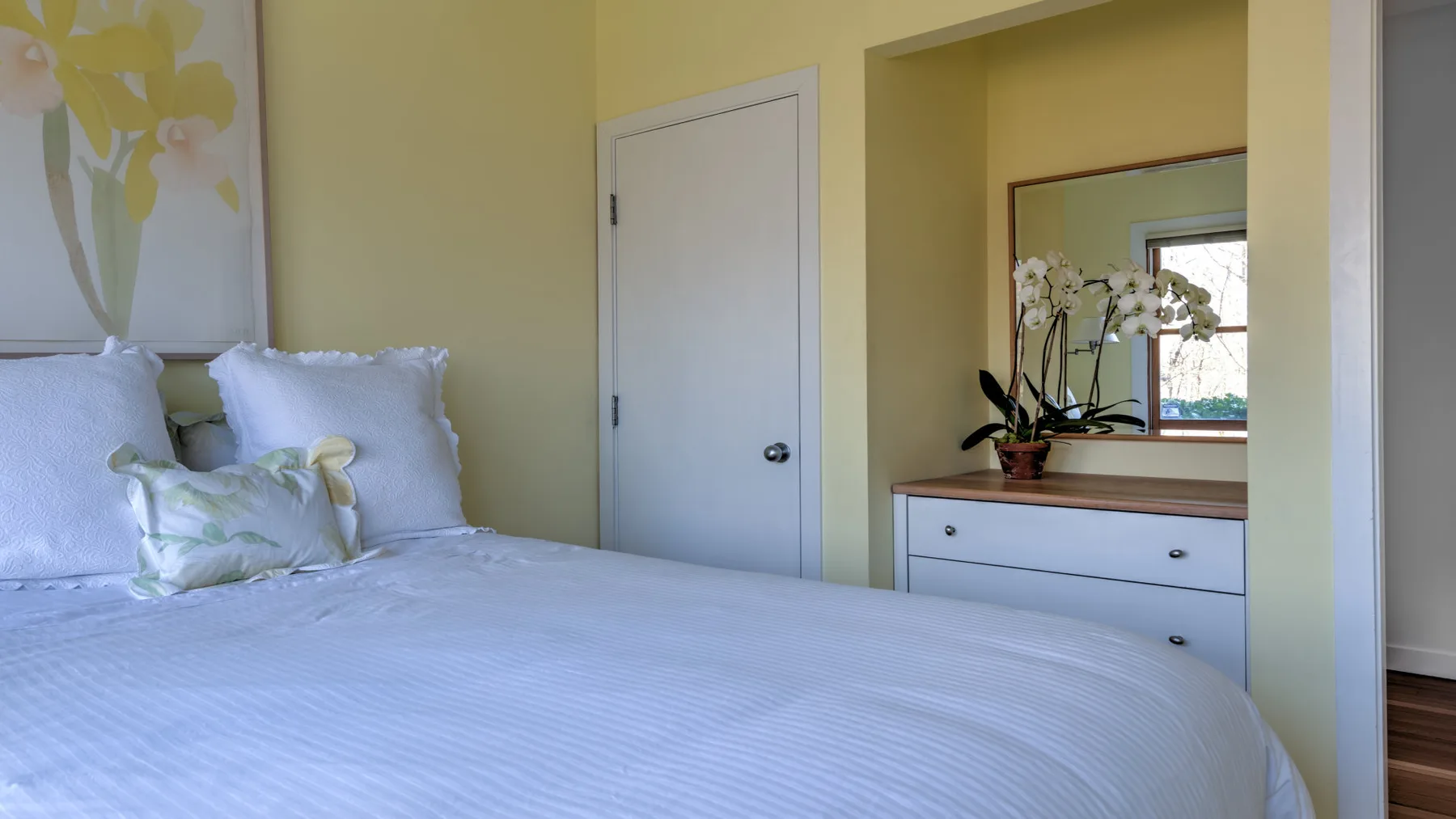 A bedroom with a neatly made bed and a dresser beneath a mirror.