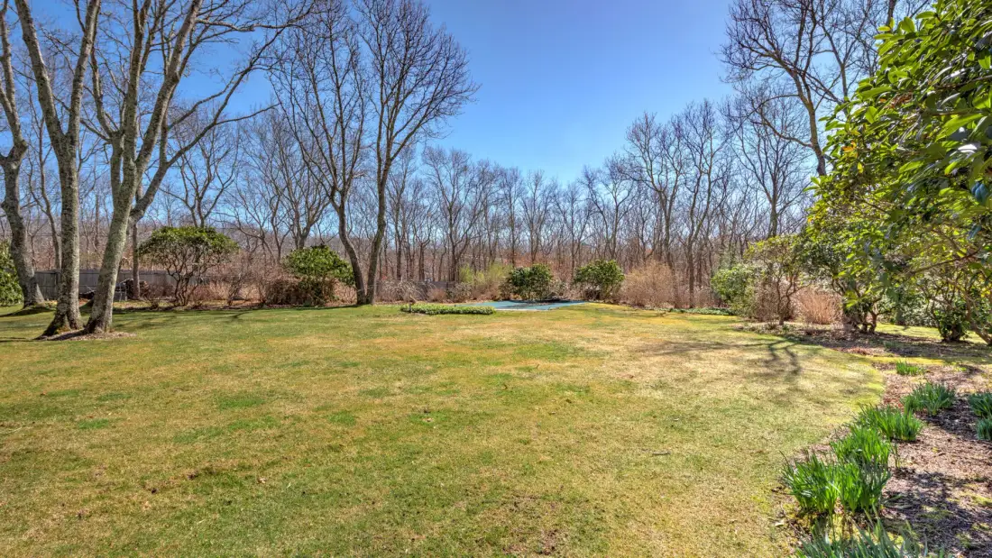 A grassy yard bordered by trees and shrubs under a clear sky.