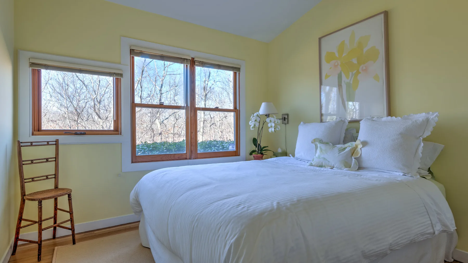 A bright bedroom with a neatly made bed and large windows overlooking trees.