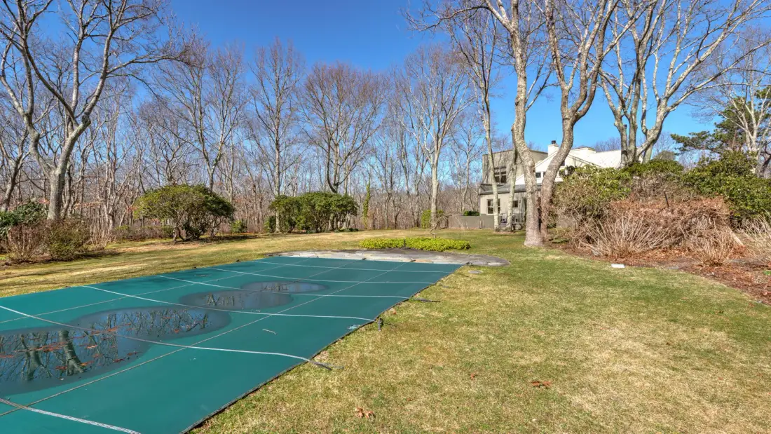 An outdoor tennis court sits beside a grassy lawn and leafless trees.