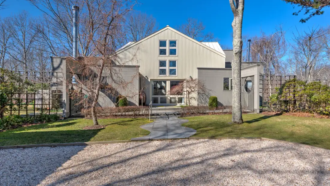 A modern house stands behind a paved path and landscaped yard.