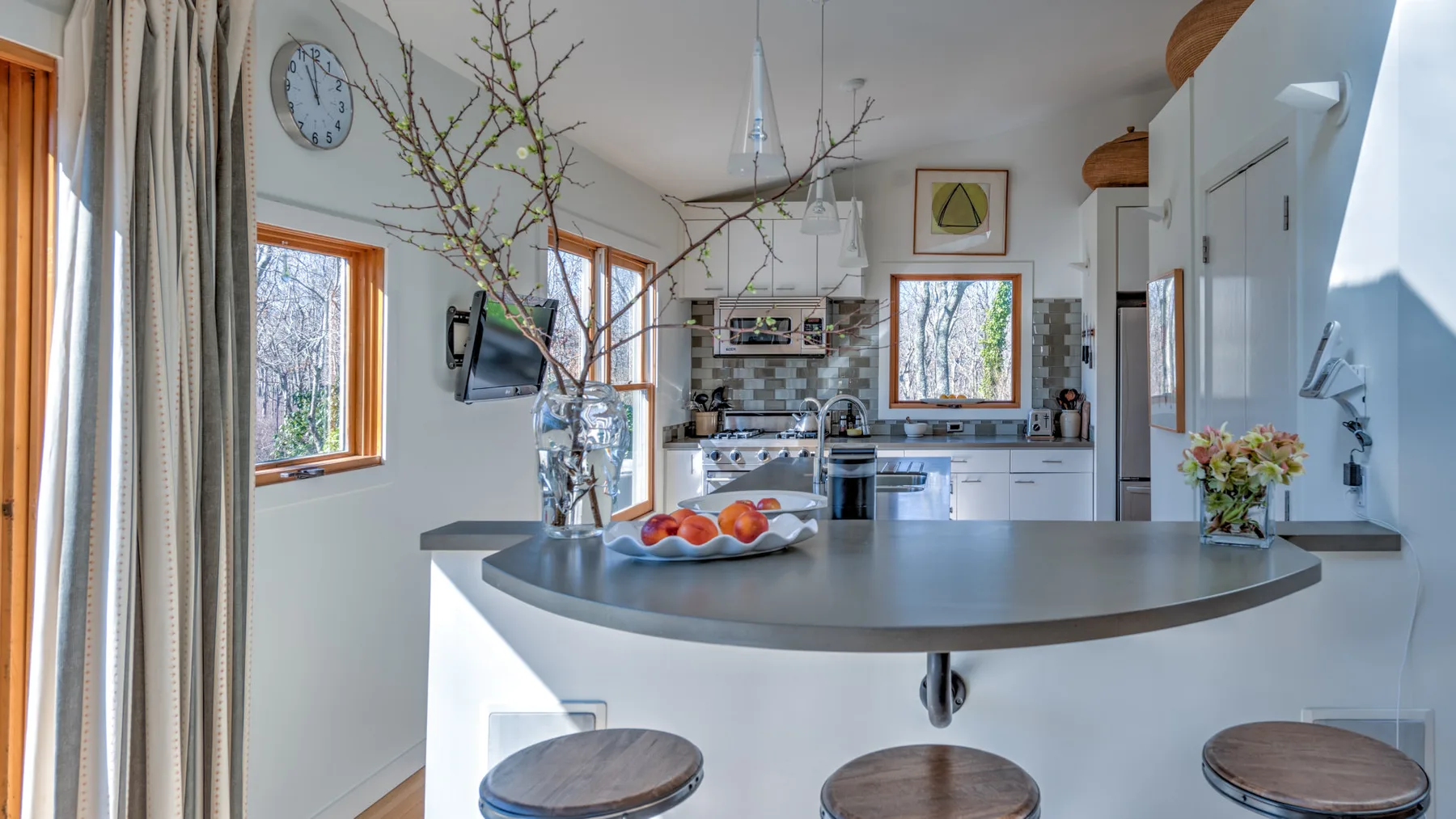 A bright kitchen with a curved island and windows overlooking trees.