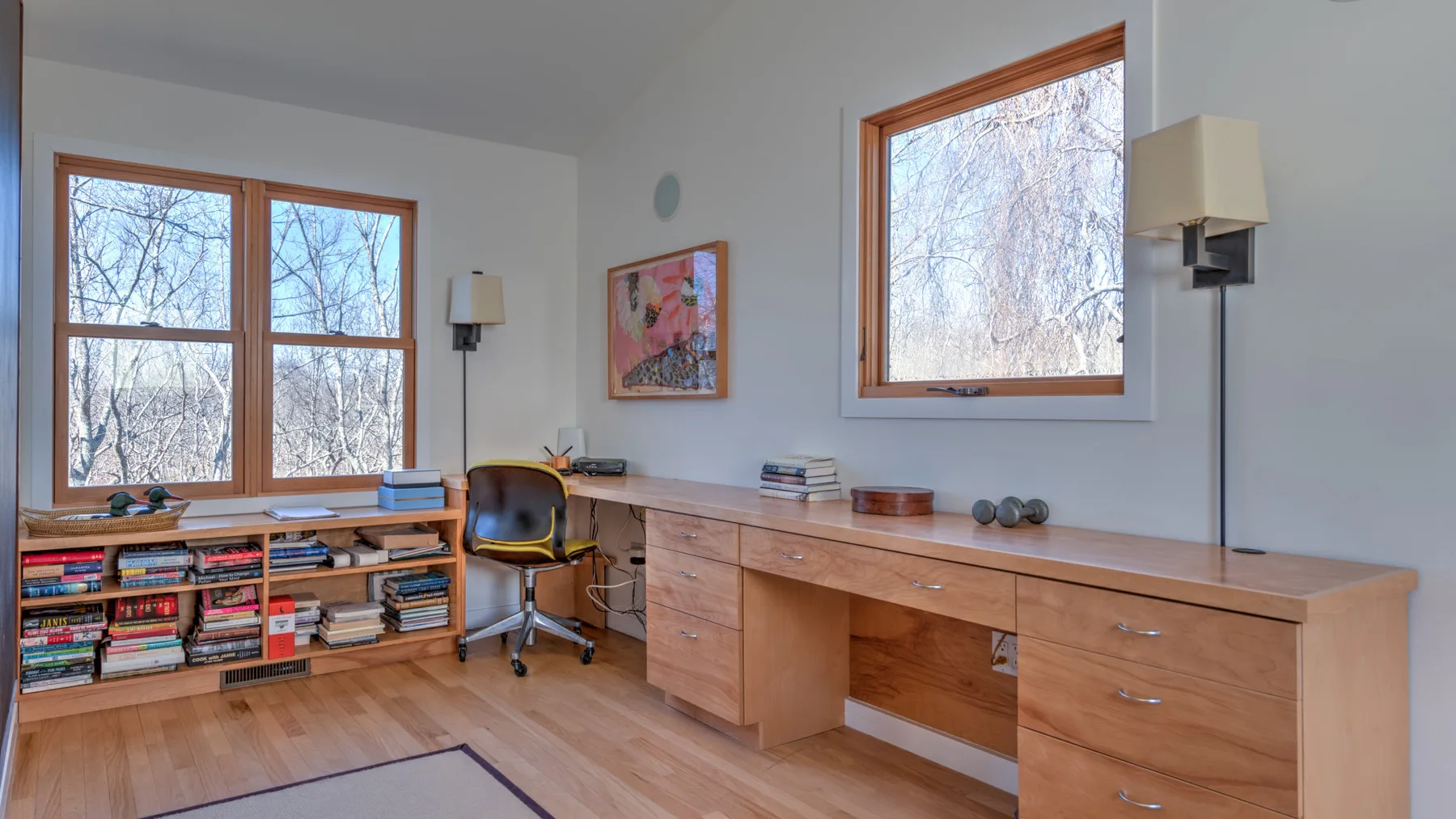 A bright study with a long wooden desk and shelves of books.
