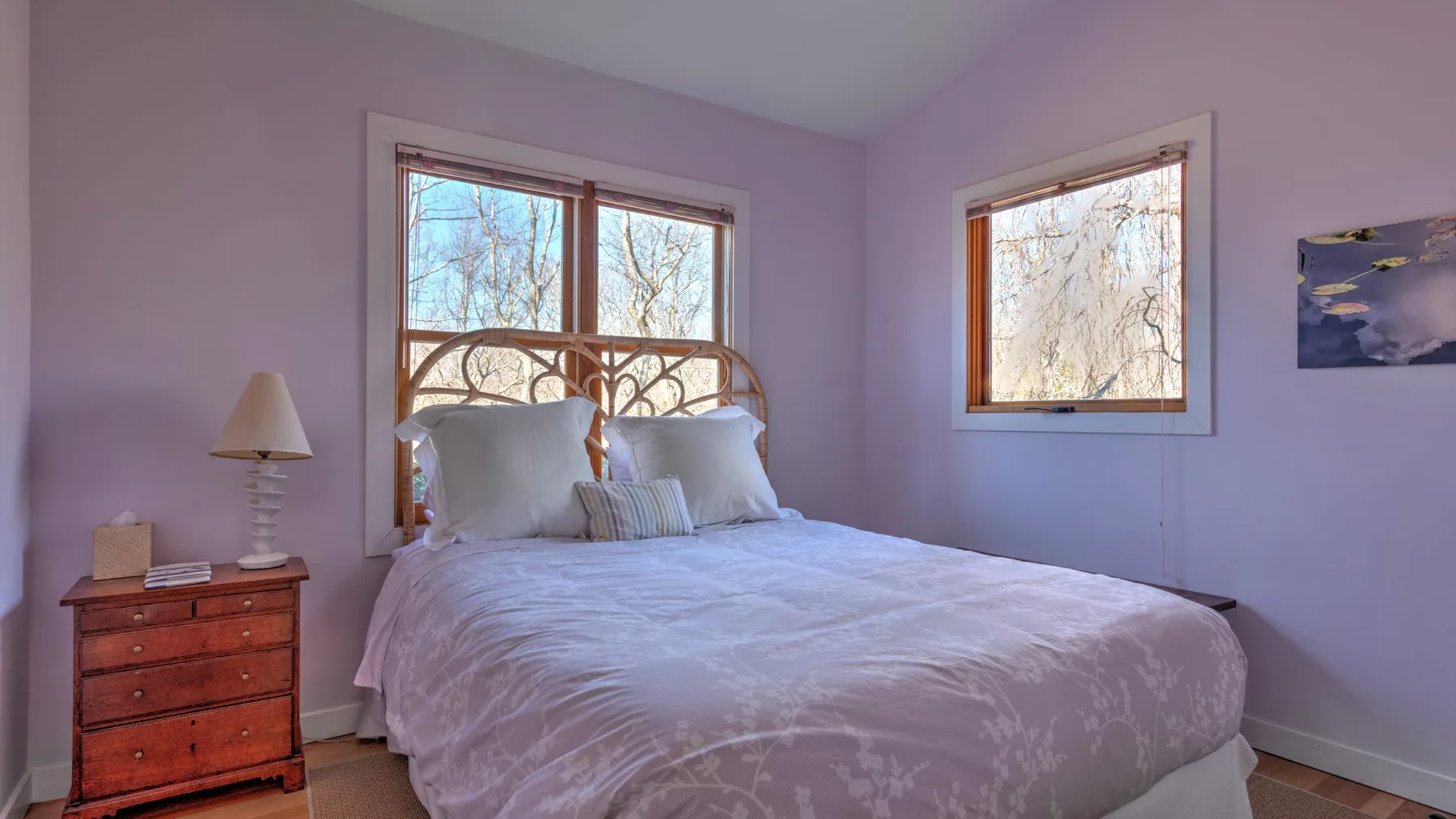 A bedroom with a bed beneath two windows overlooking leafless trees.