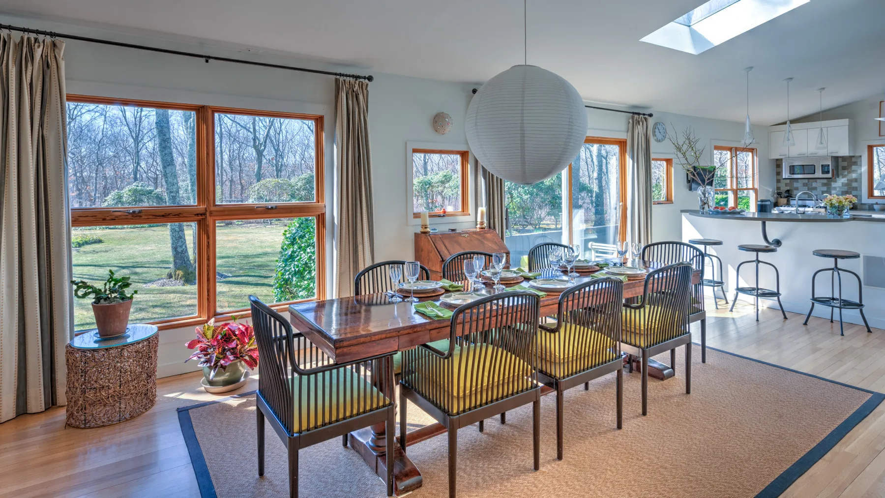 Un comedor con una mesa larga y grandes ventanas con vista a los árboles.