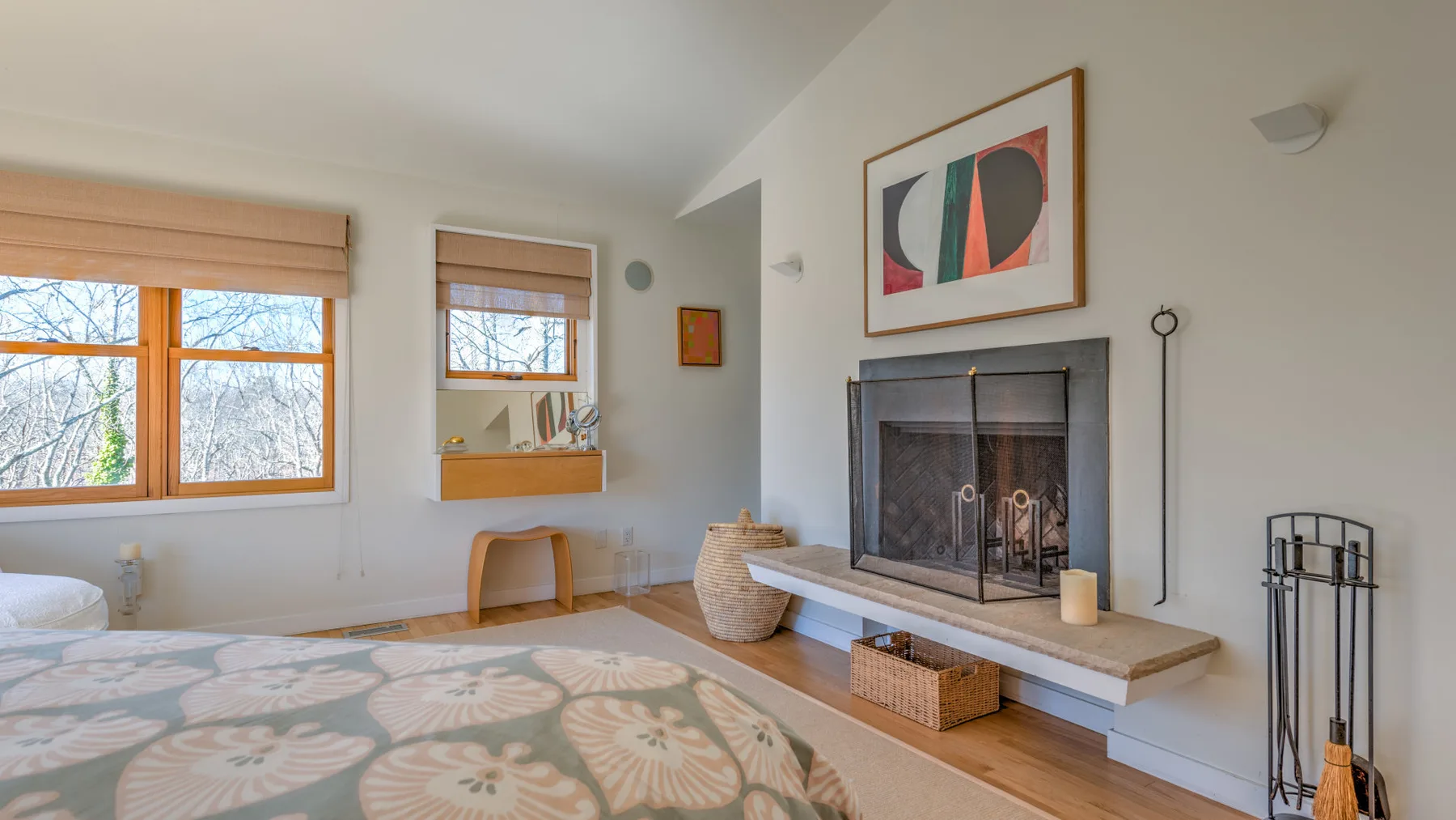 A bright bedroom with a patterned bedspread, windows, and a fireplace.