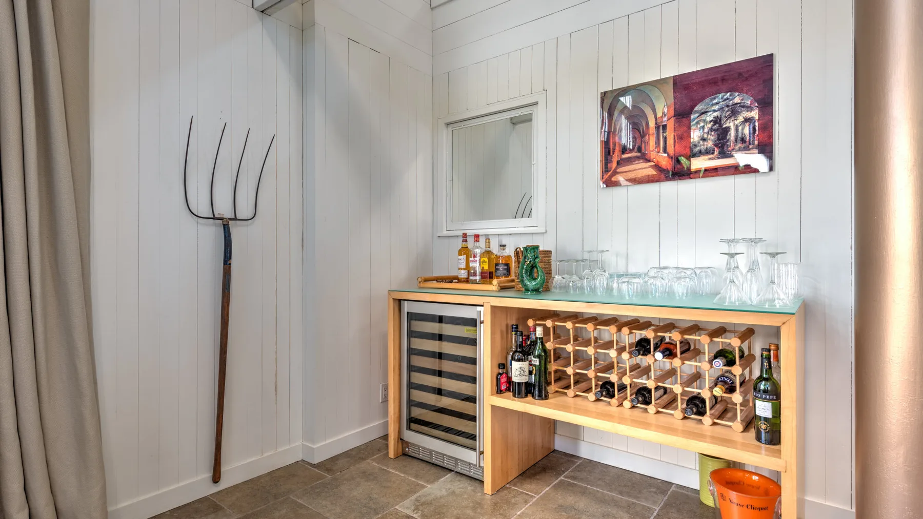 A small bar area with a wooden wine rack, bottles, and glassware.