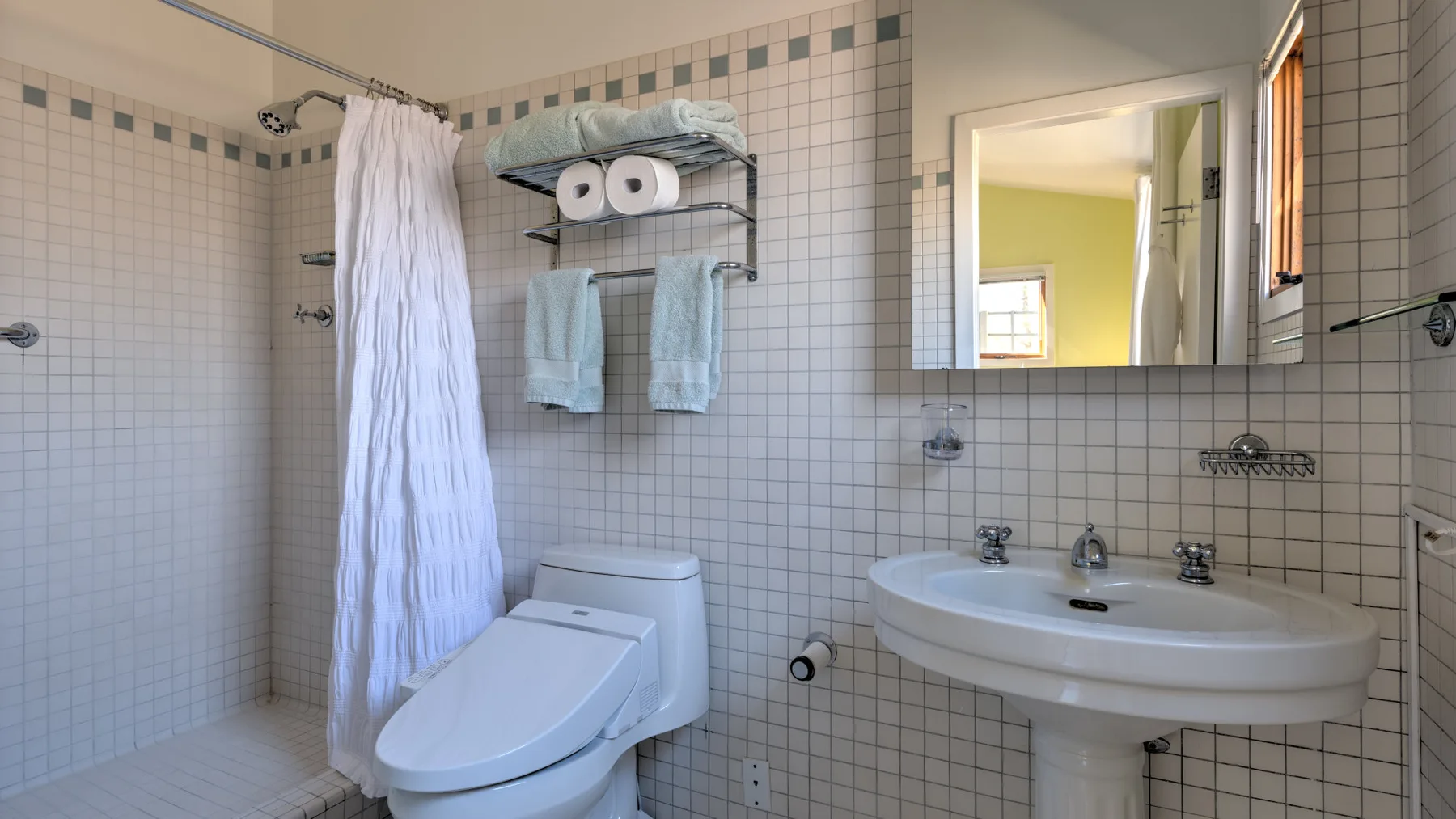 A tiled bathroom with a shower curtain, toilet, and sink.