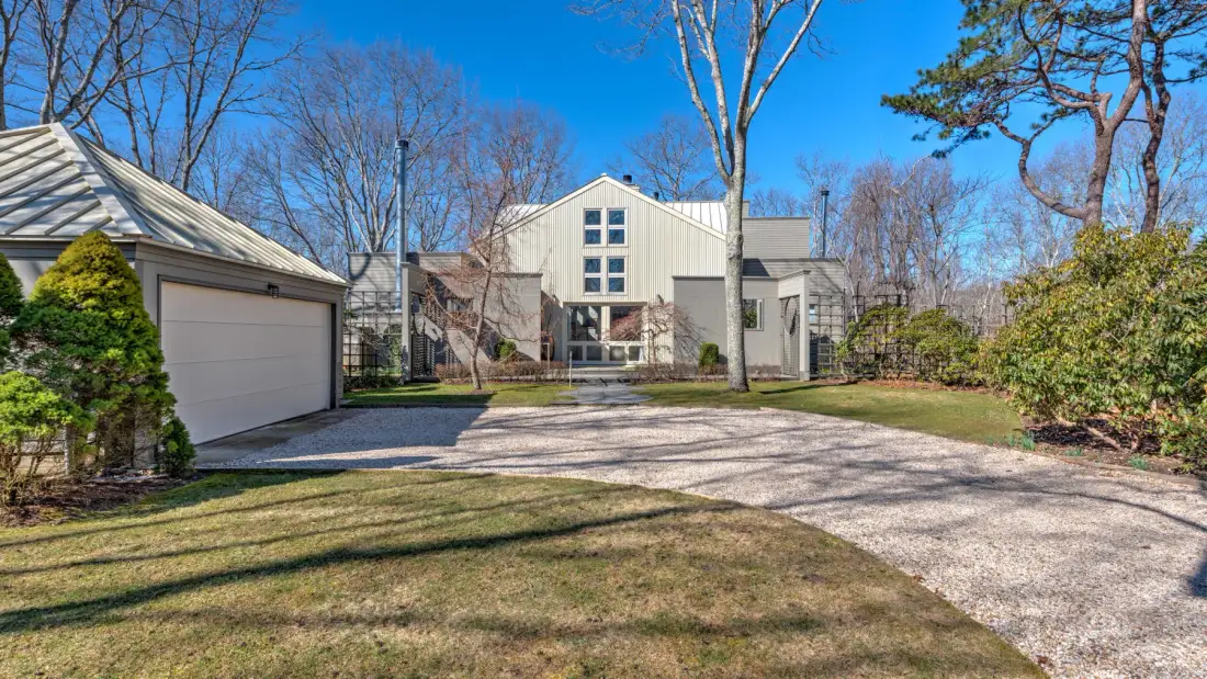 A modern house stands beyond a curved gravel driveway, with trees around the yard.