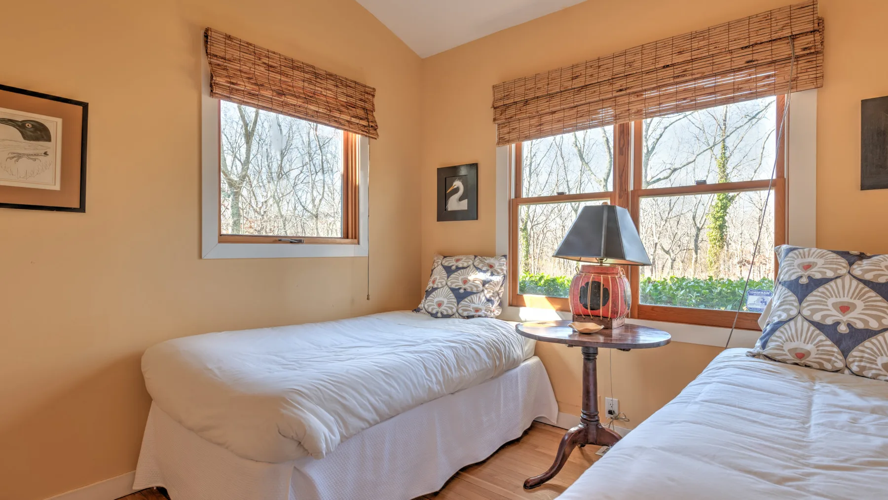 A bedroom with two beds and large windows overlooking trees.