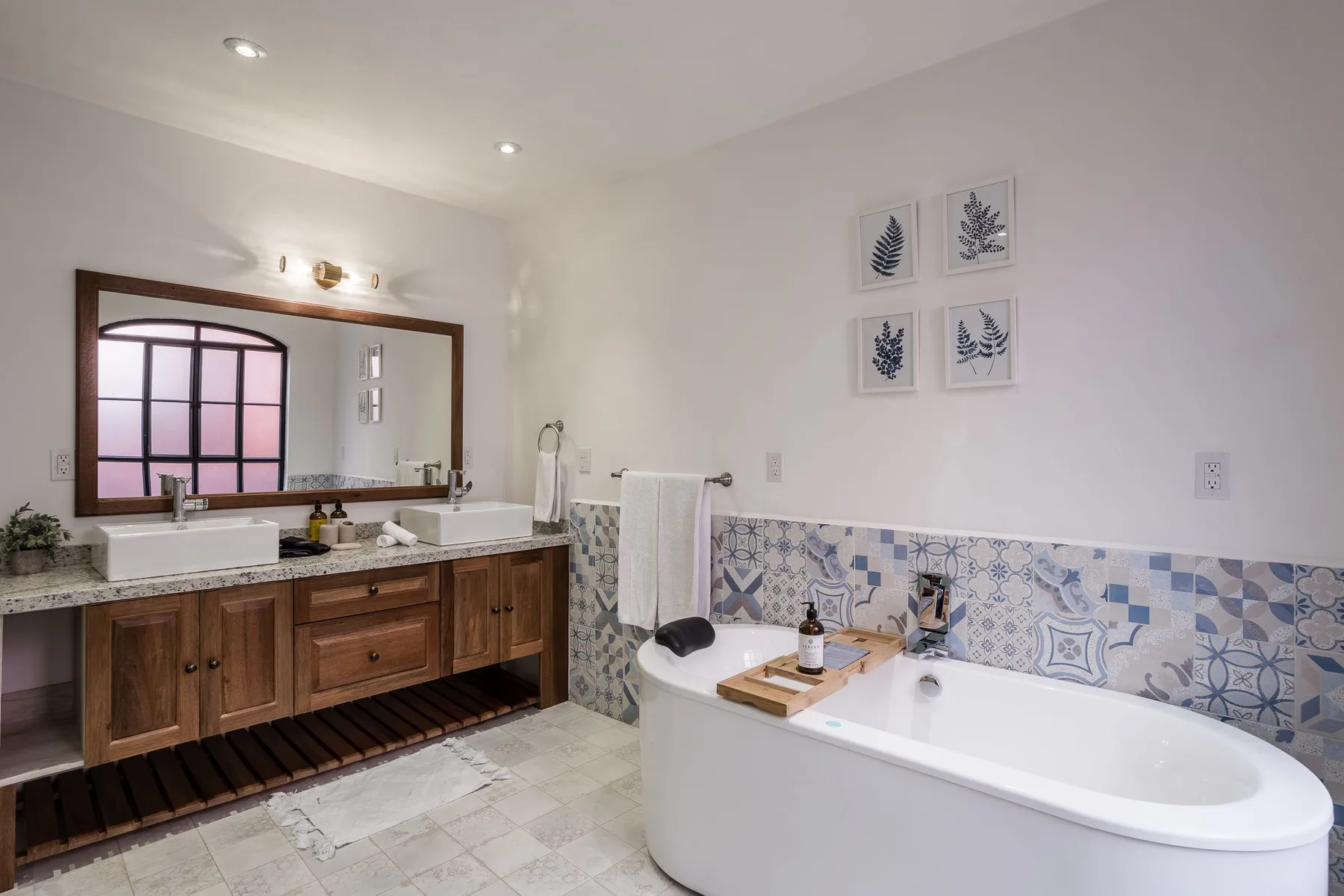 A bright bathroom with a double sink vanity, bathtub, and patterned tile.