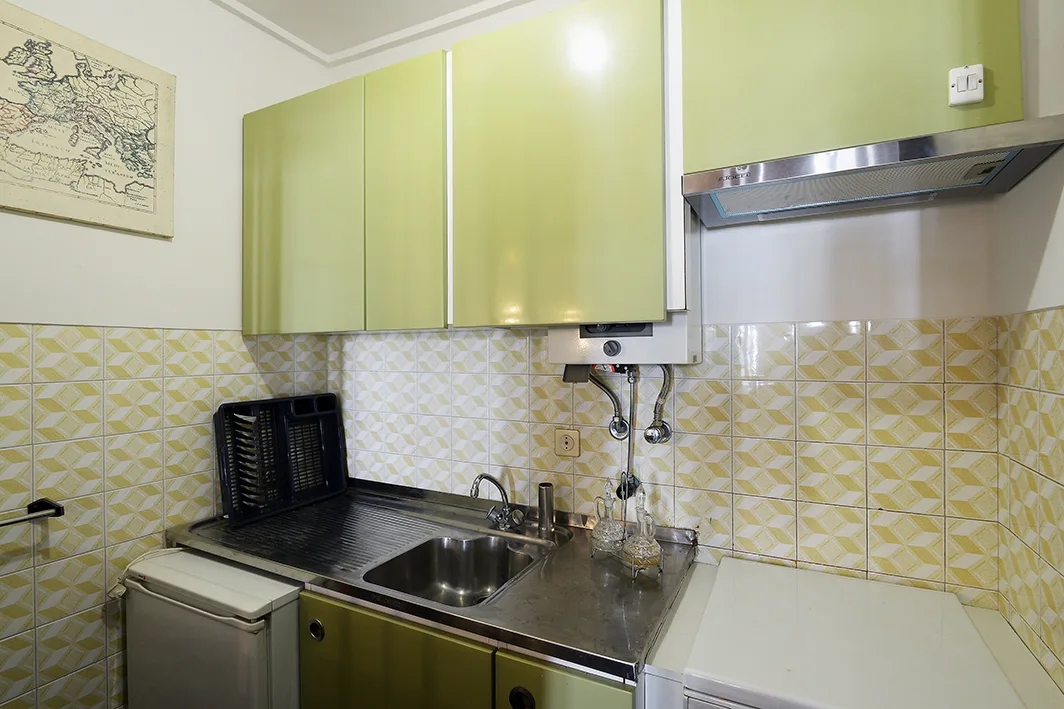 Una cocina compacta con fregadero de acero inoxidable y armarios verde claro.