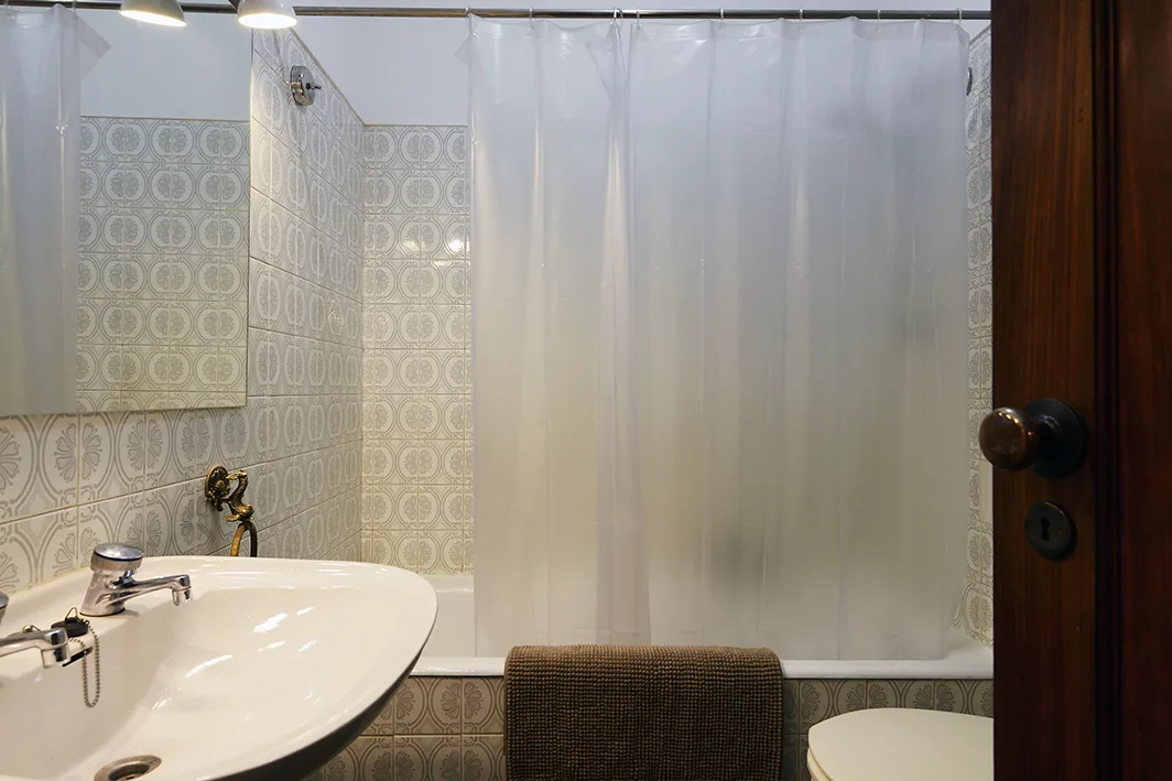 Un baño con lavabo, paredes de azulejos estampados y una cortina de ducha.