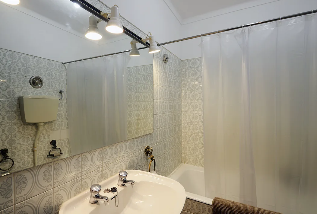 Un baño con lavabo, azulejos estampados y una cortina de ducha.