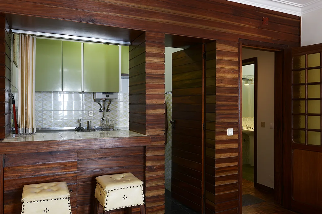 Una pequeña barra de cocina con taburetes está junto a una puerta con paneles de madera oscura.