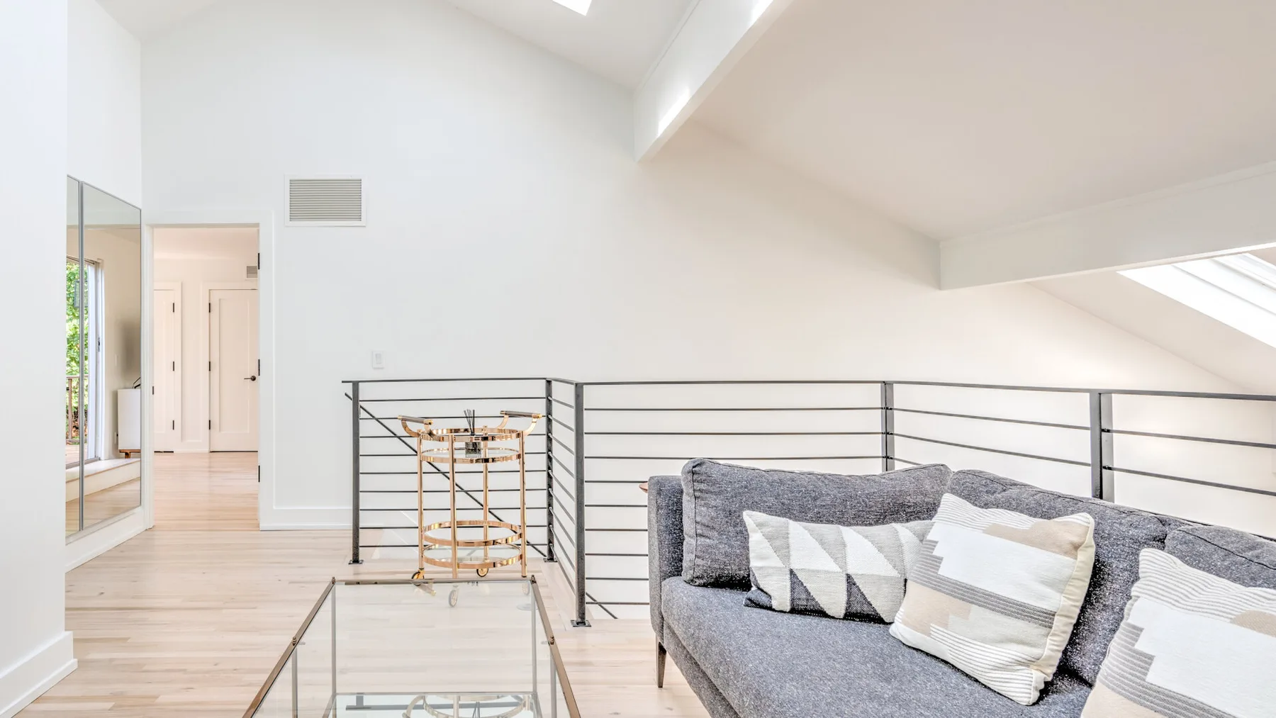 Una luminosa sala tipo loft con un sofá gris junto a una barandilla metálica.